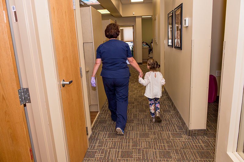 Pediatric Dental Associates employee leading a young patient to her chair